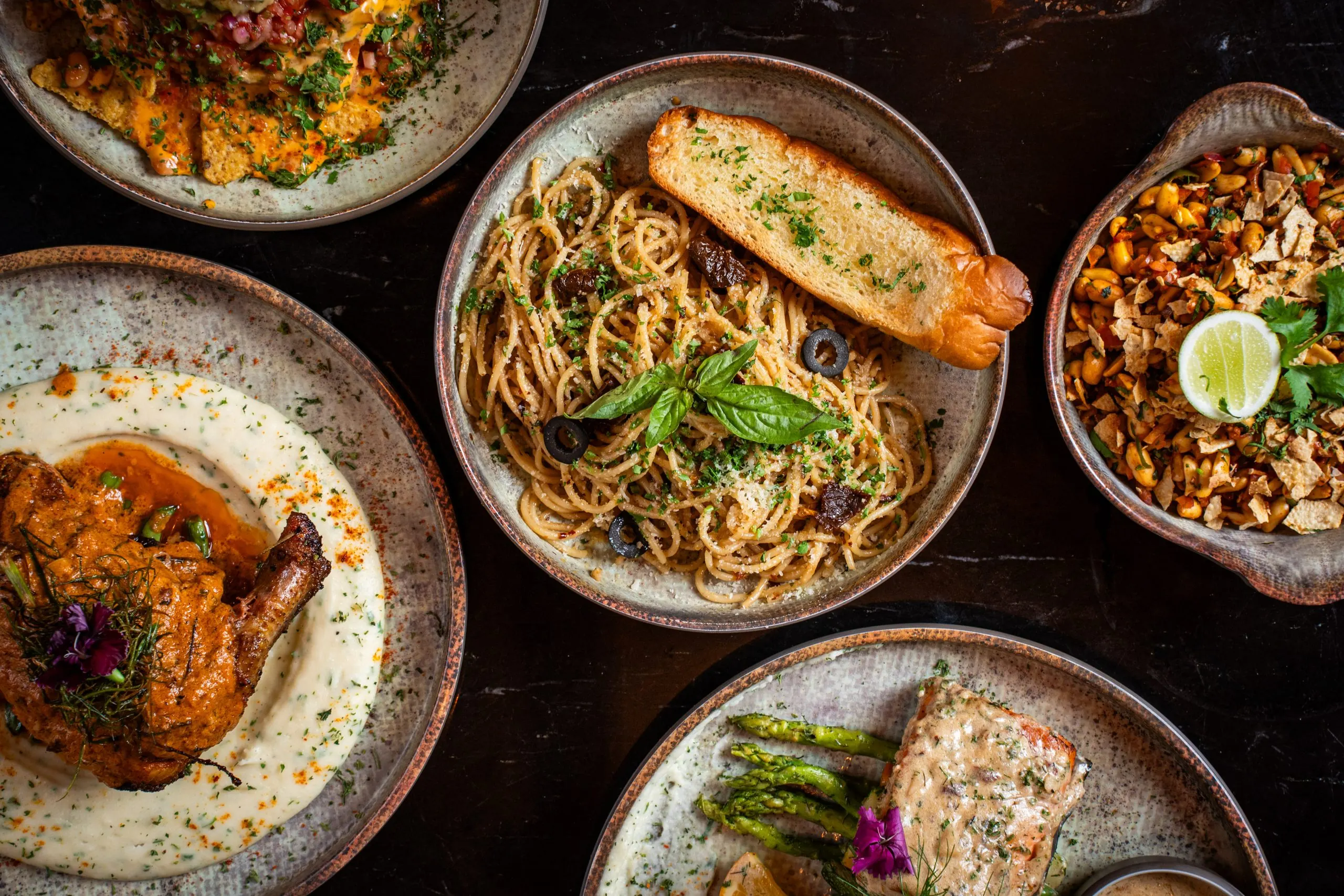 Pasta, garlic bread and small plates from Ālaya's kitchen on a dark marble table