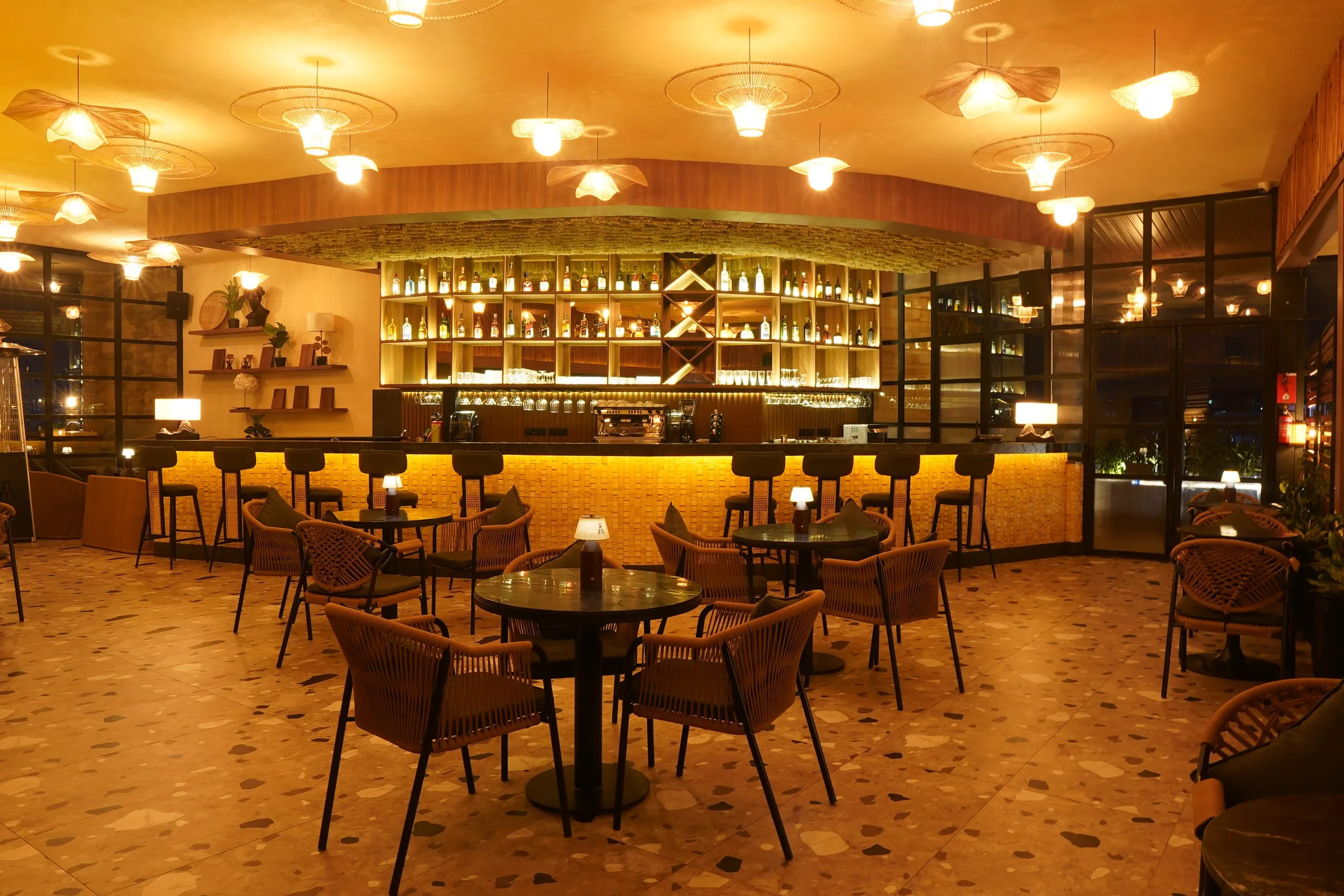 Ālaya's bar and lounge at night, woven pendants above rattan chairs