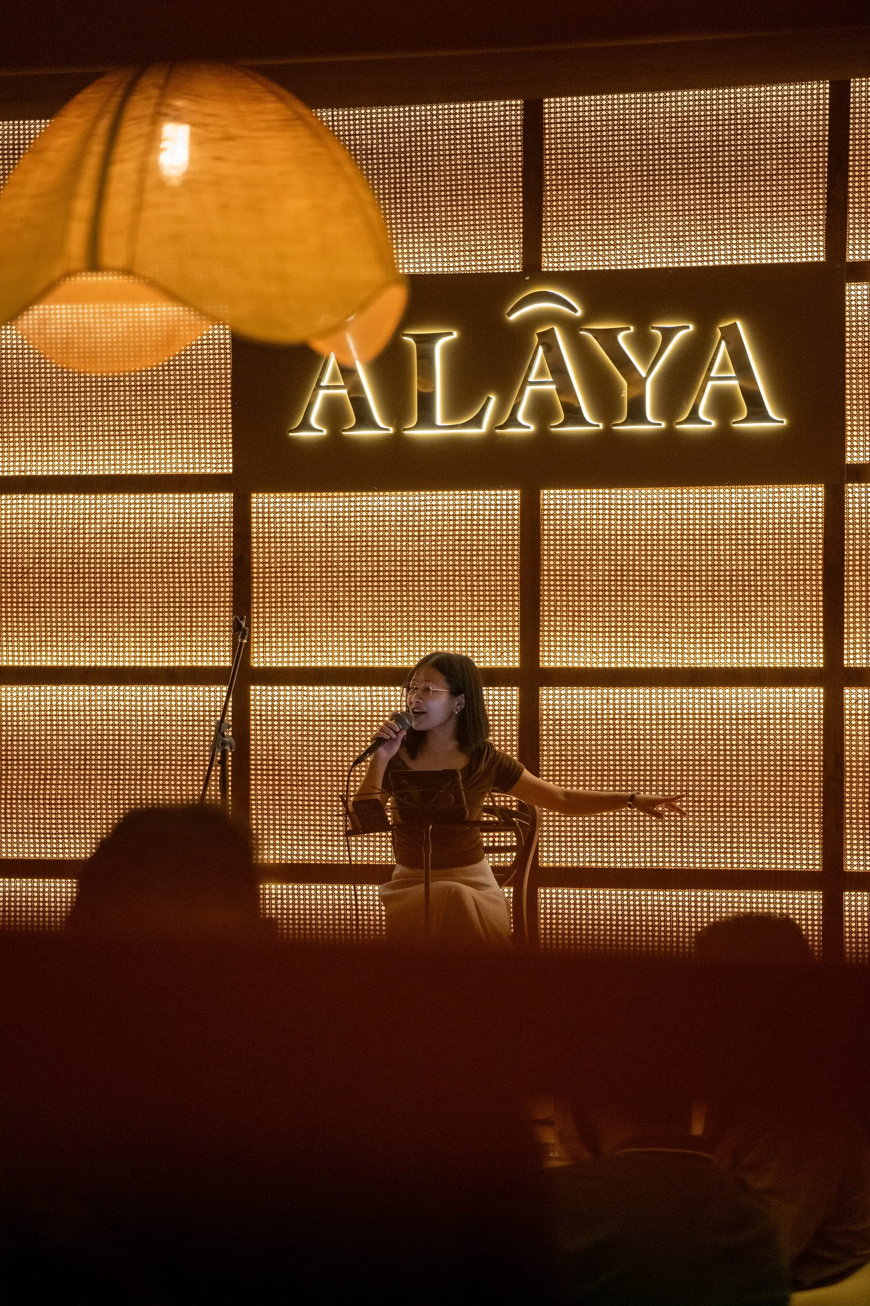 A performer on Ālaya's stage in front of the lit Ālaya sign