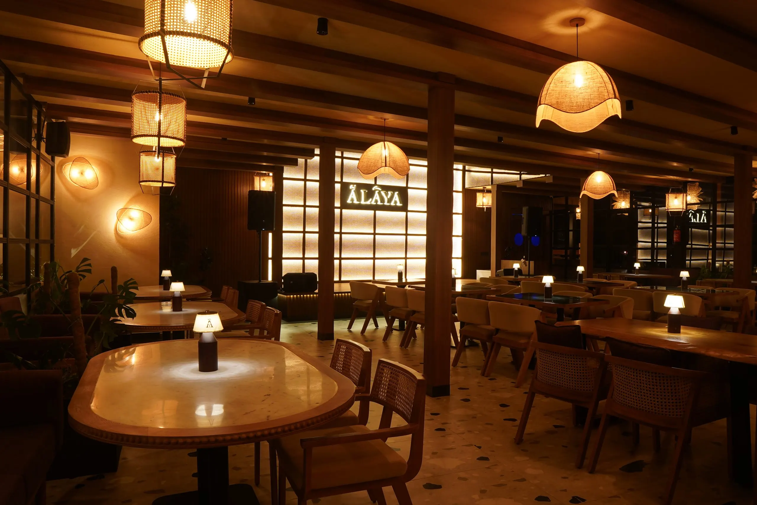 A round table under a single lamp at Ālaya at night, with the lit Ālaya window behind