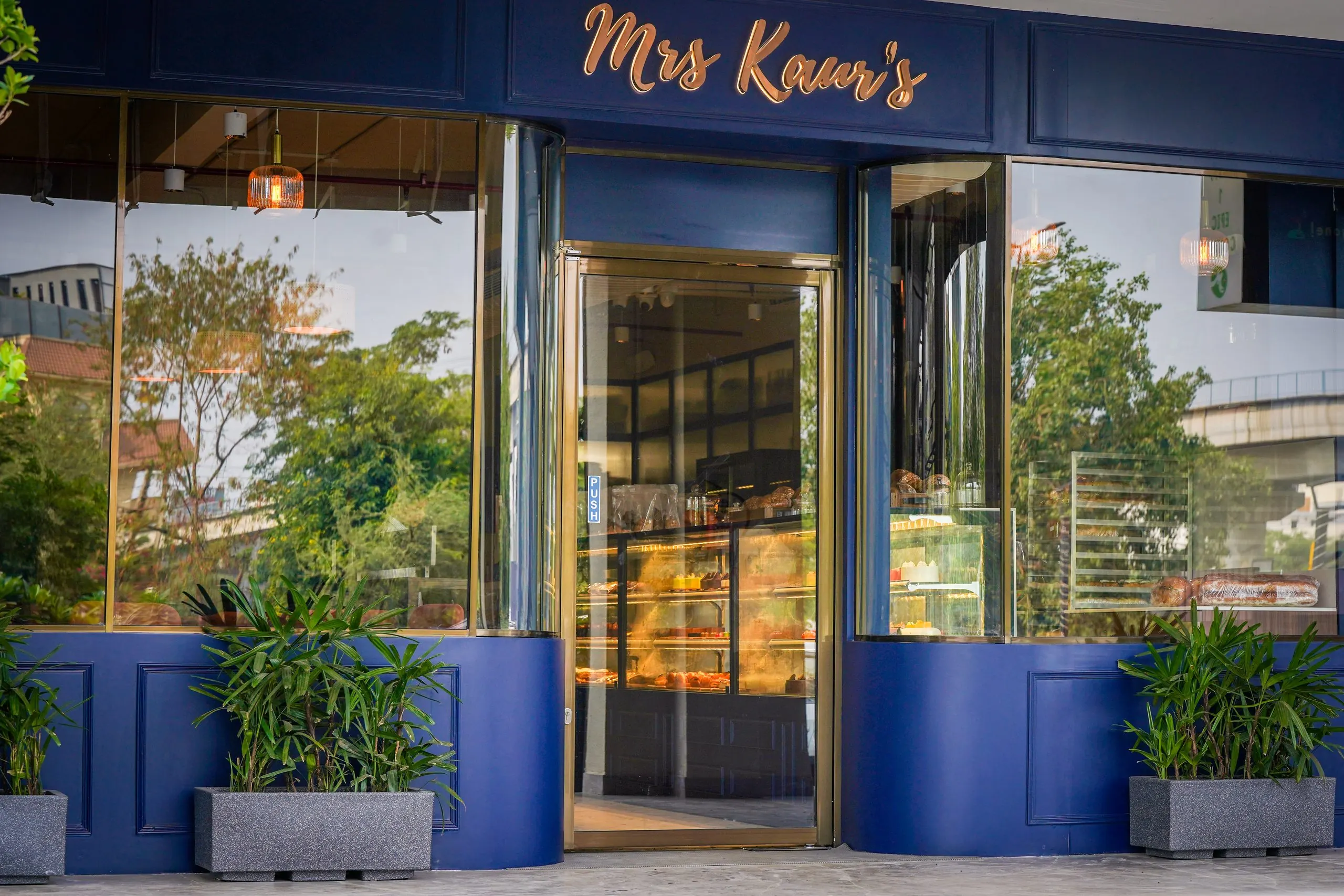 The navy shopfront of Mrs Kaur's on Golf Course Road, Gurugram, with gold lettering and planting
