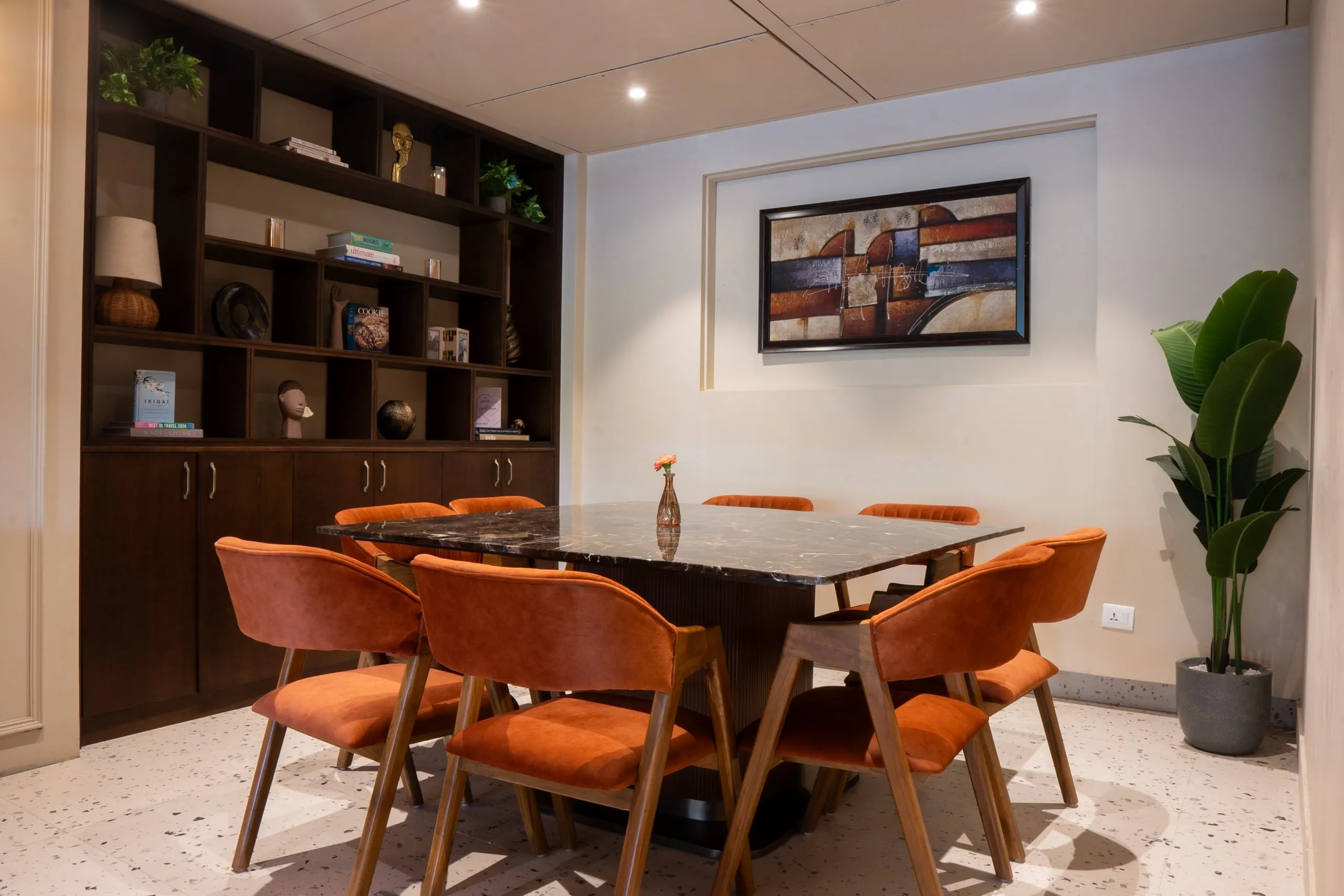 Rust-coloured chairs around the table, in front of dark timber shelving