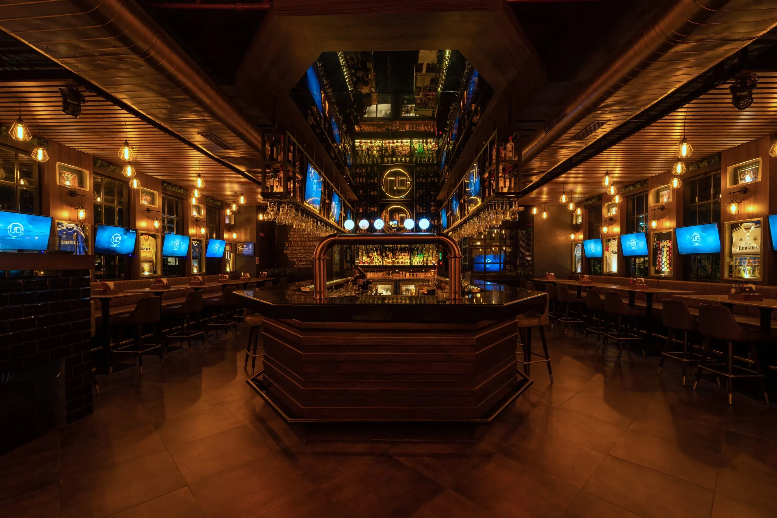 The central island bar at Underdoggs Aerocity under a timber ceiling