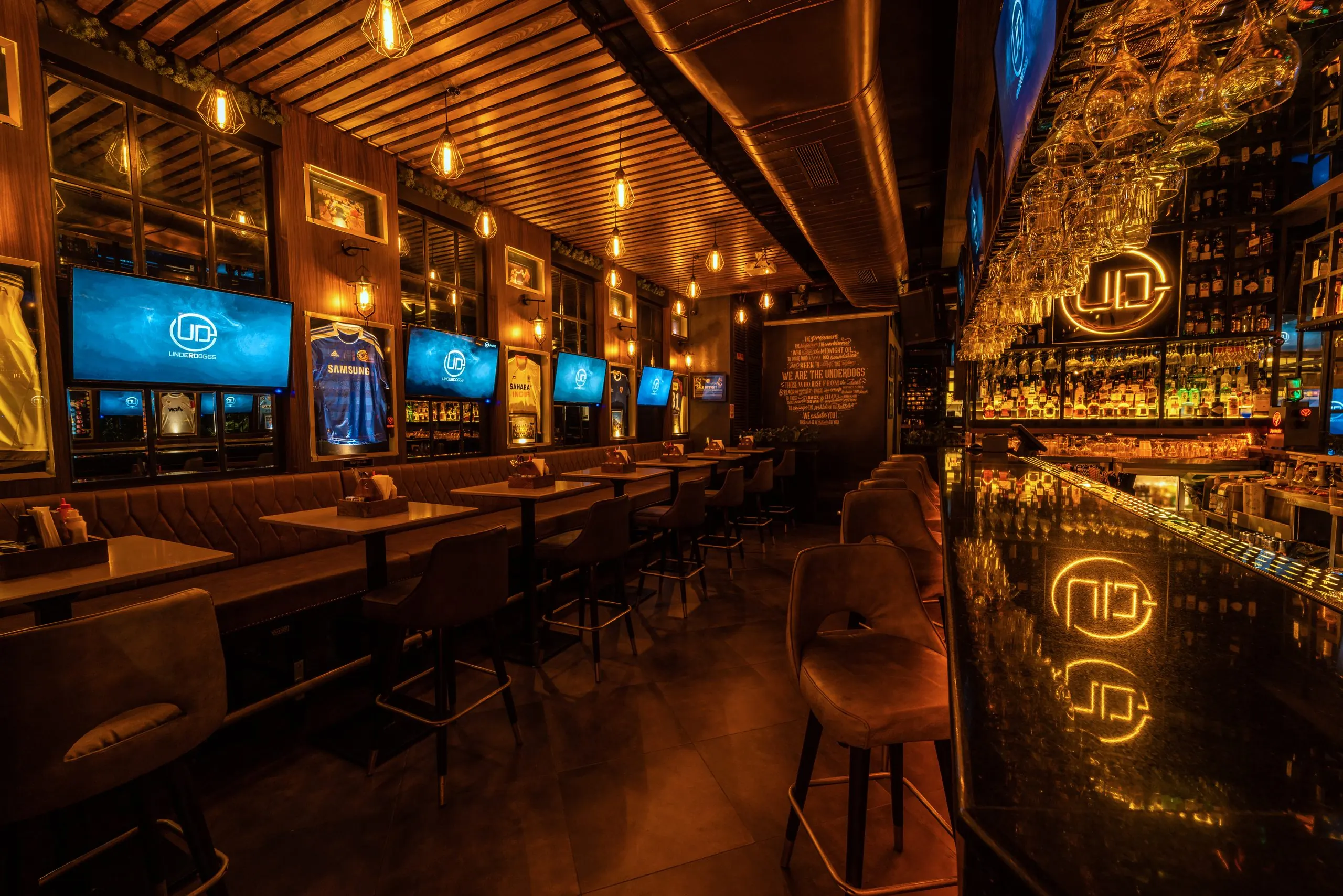 The long bar at Underdoggs Aerocity, back-lit shelving reflected in the counter