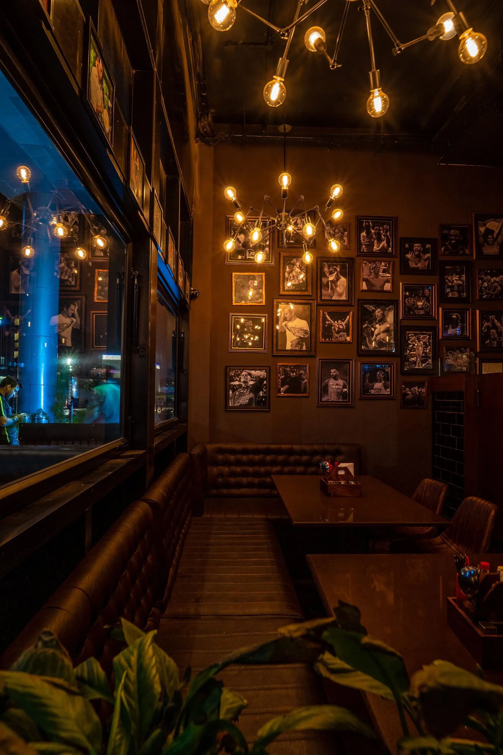 A window booth at Underdoggs Aerocity: leather banquettes under framed sports photographs and bare-bulb chandeliers