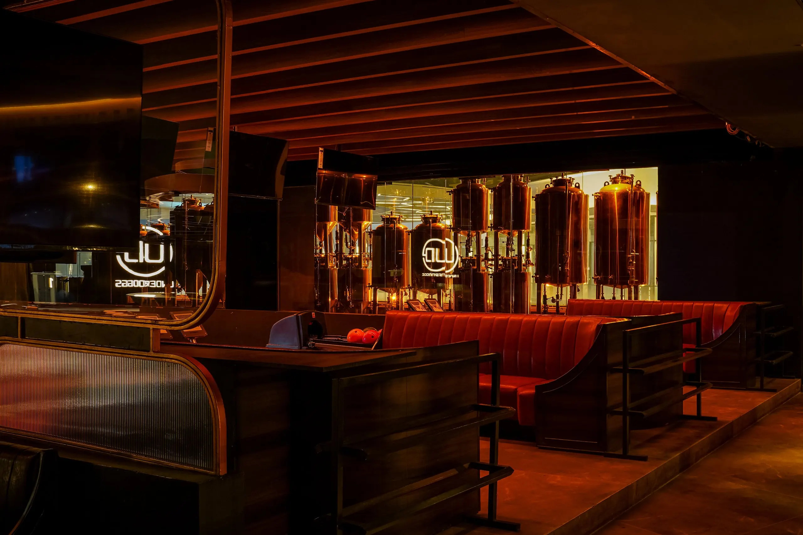 The copper brewhouse behind glass at Underdoggs Arena, the brand's Gurugram flagship, with red leather booths in front