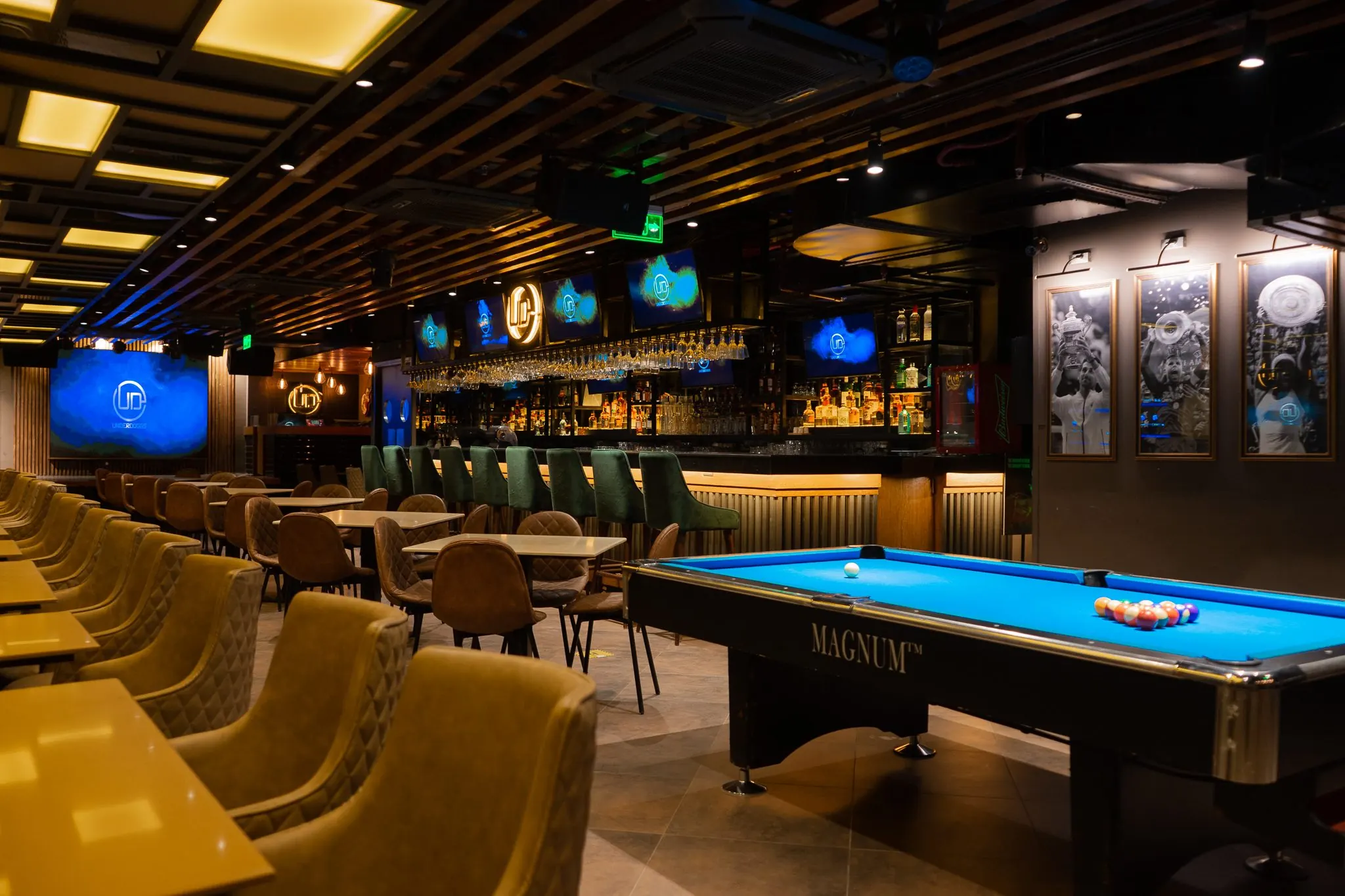 Pool table and bar at Underdoggs Cyber Hub, with framed black-and-white tennis photographs on the wall