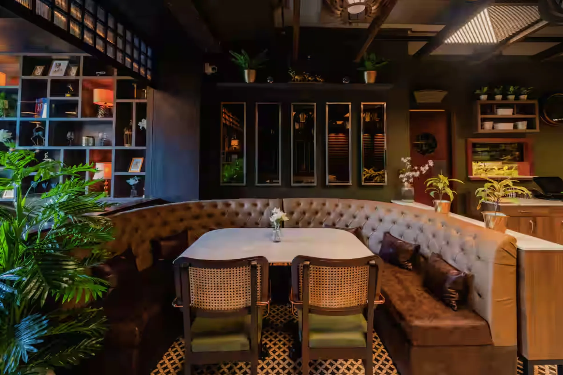 A curved tufted leather booth at Uptown Escape, with rattan chairs, a marble table, display shelving and planting