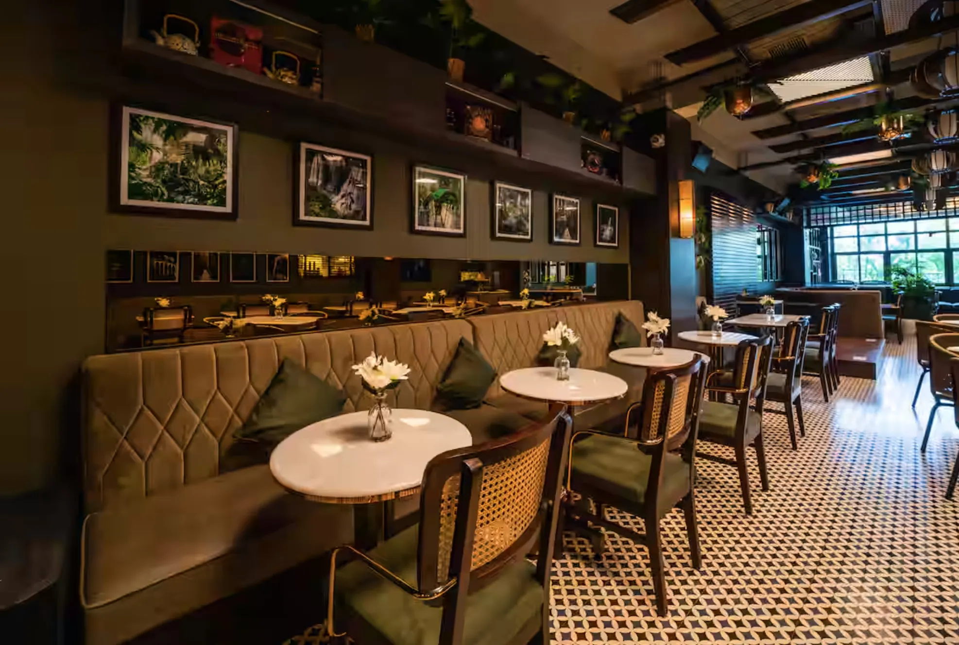 A long quilted banquette at Uptown Escape with round marble tables, rattan chairs with olive cushions and a black-and-white tiled floor